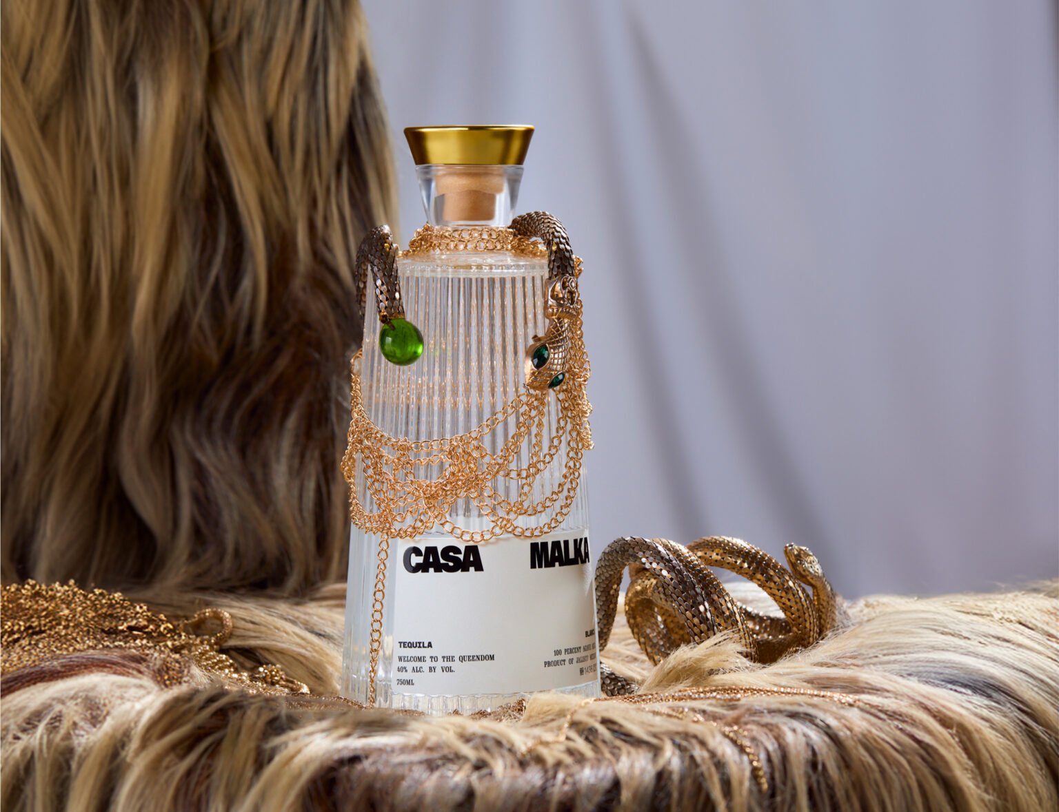 Casa Malka Tequila bottle adorned with gold necklaces, set against a luxurious fur backdrop