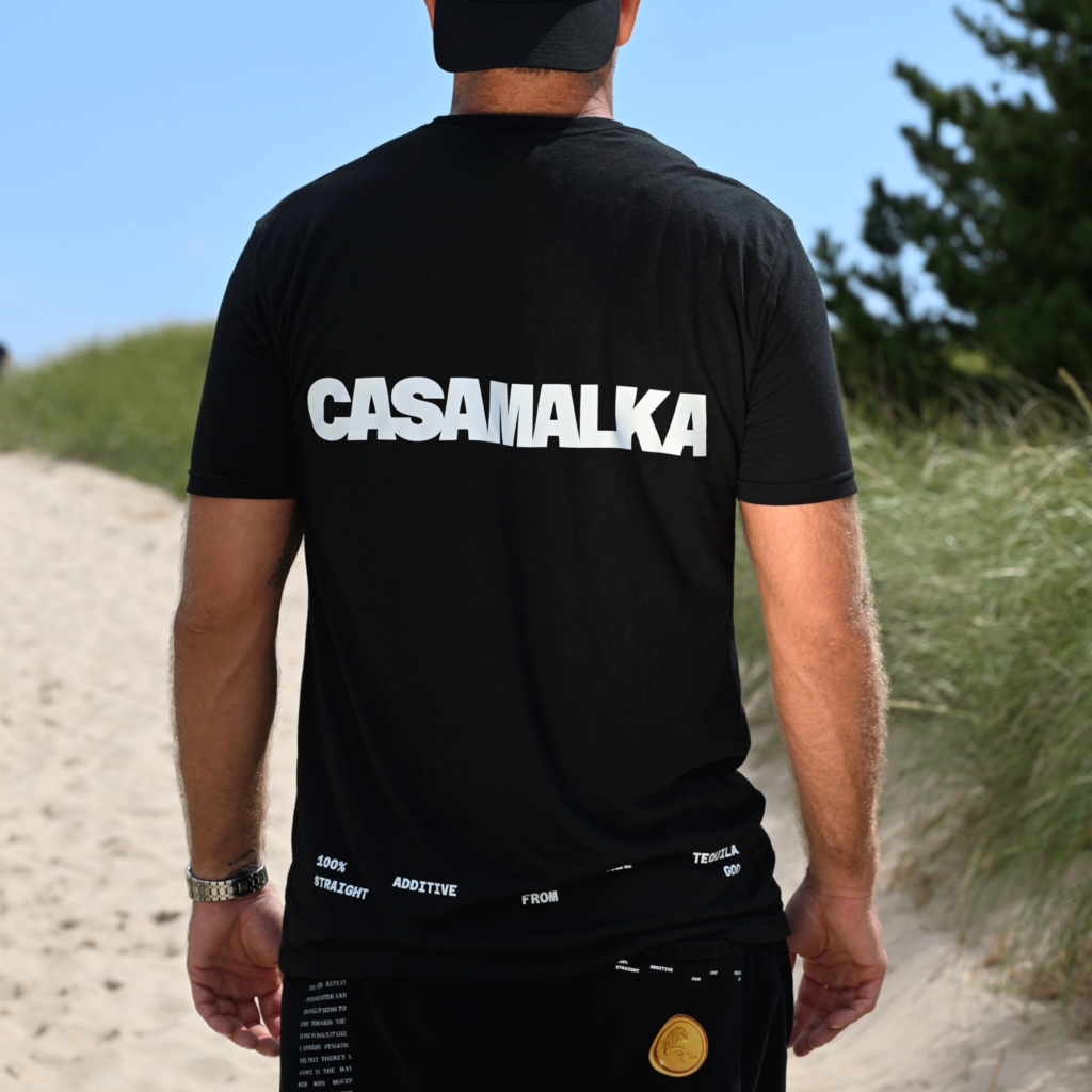 Back view of man wearing black Casa Malka t-shirt with bold logo design