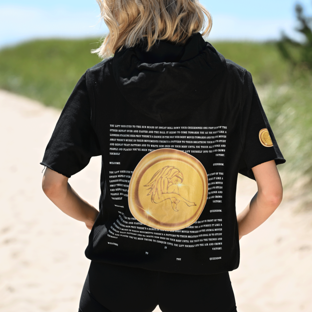 Back view of woman in black Casa Malka hoodie, featuring large gold coin design